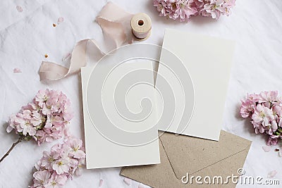 Wedding stationery mock-up scene. Blank greeting cards, envelope on linen tablecloth background with pink blossoming Stock Photo