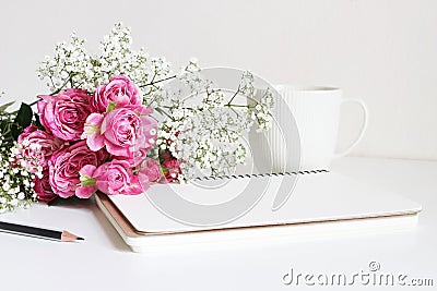 Wedding styled stock photo. Still life with pink roses, baby`s breath Gypsophila flowers, white cup, pencil and notebook Stock Photo