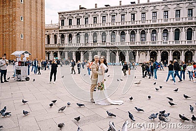 Wedding in Venice, Italy. Bride and groom are looking at camera among the pigeons in Piazza San Marco, against backdrop Editorial Stock Photo