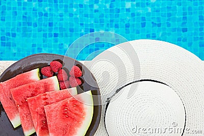 Wedges of Ripe Juicy Seedless Watermelon Raspberries on Plate on Rattan Table by Swimming Pool. Vacation Relaxation Summer Stock Photo