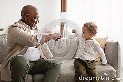 Happy Black Grandpa And Little Grandson Bumping Fists At Home Stock Photo