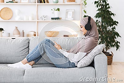 Weekend Pastime. Arabic girl relaxing at home with smartphone and wireless headphones Stock Photo