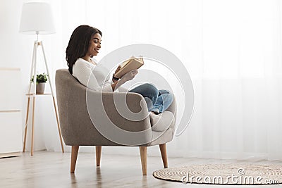 Weekend pastime. Relaxed african american woman reading book in comfortable armchair against window, free space Stock Photo