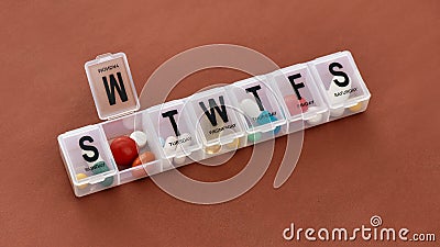 A weekly medicine dispenser opened for Monday, prescription pills and vitamins in a white pill box on terracotta Stock Photo