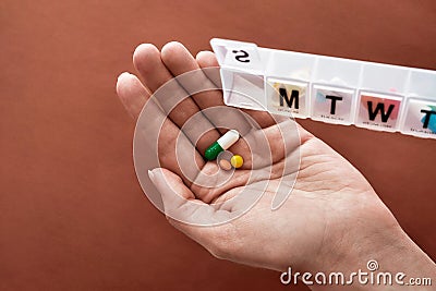 A weekly medicine dispenser opened for Sunday, hand holding pills and vitamins from white pill box on terracotta Stock Photo