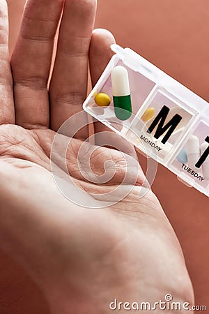 A weekly medicine dispenser opened for Sunday, hand taking pills and vitamins out of white pill box on terracotta Stock Photo