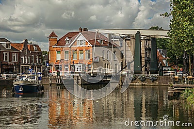 Boat passing by bascule bridge raised on tree-lined wide canal in cloudy day at Weesp. Editorial Stock Photo