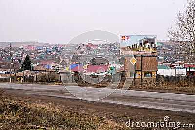 Welcome board before entering the city of Uzhur from the south, against the backdrop of rural houses. Editorial Stock Photo