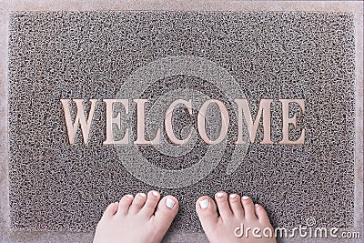 Welcome Door Mat With Female Feet. Friendly Grey Door Mat Closeup with Bare Woman Feet Standing. Welcome Carpet. Stock Photo