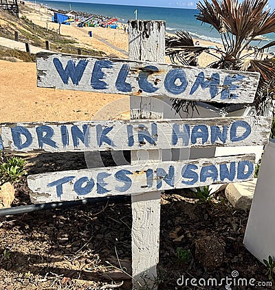 Welcome, drink in hand, toes in sand, beach sign Stock Photo