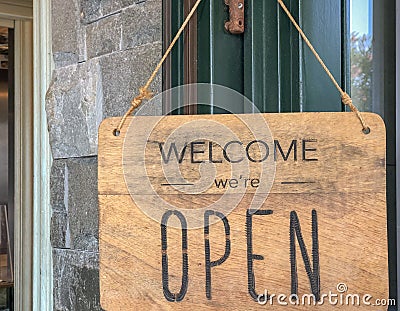 Welcome, we are open sign on the door of the store/cafe. Wooden board with text. Business after quarantine concept. Stock Photo
