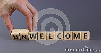 Welcome or unwelcome symbol. Businessman turns wooden cubes and changes the word unwelcome to welcome. Beautiful grey table, grey Stock Photo