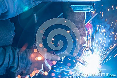 Welder welding metal with argon arc welding machine and has welding sparks. A man wears welding mask and protective gloves. Safety Stock Photo