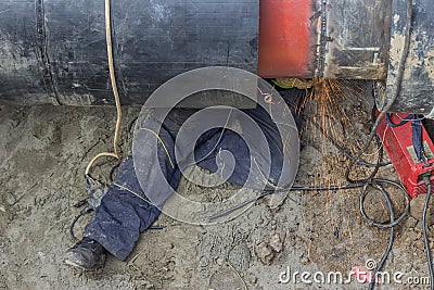 Welder worker grinding the weld in trench under pipeline Stock Photo