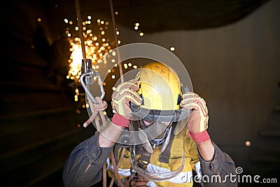 welder worker hanging working at height wearing helmet using face shield safety equipment protection Stock Photo