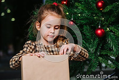 Well behaved girl sitting under a christmas tree, looking at wrapped present Stock Photo