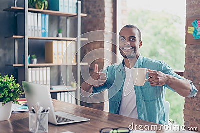 Well done! Successful happy afro student is showing thumb up sign. He is handsome, smiling, in casual wear, at his work station Stock Photo