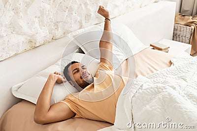 Wellslept Middle Eastern Man Awakening Stretching Arms Lying In Bedroom Stock Photo