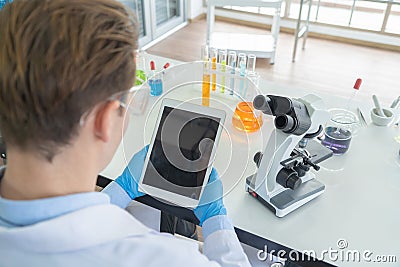 A western scientist man holding blank space tablet, working on test tube to analysis and develop vaccine of covid-19 virus in lab Stock Photo