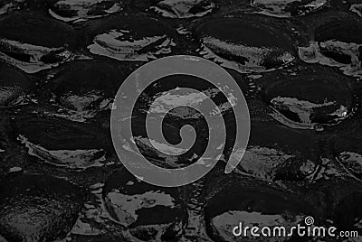 Wet black cobblestone pavement of smooth volcanic cobble with reflection, texture, top view, closeup, background. Stock Photo