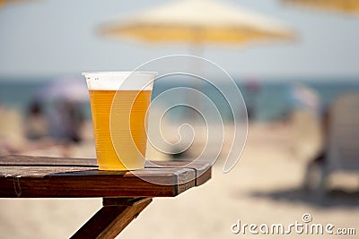 Wet glass of golden cool tasty beer on the wooden table on the shore of the sea or ocean on the sunset. Concept of beach Stock Photo