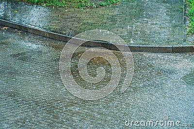 Wet sidewalk and roadway in the city after the rain. Water splashes on the road during a downpour. Large raindrops on the surface Stock Photo