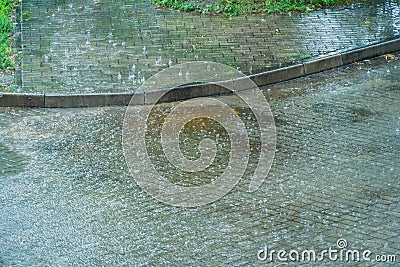 Wet sidewalk and roadway in the city after the rain. Water splashes on the road during a downpour. Large raindrops on the surface Stock Photo