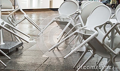 Wet white plastic chairs with raindrops in a street cafe, overturned, after a rain in Italy, in the evening Stock Photo