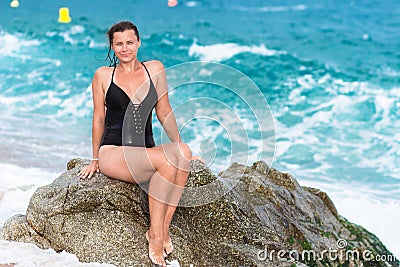 Wet woman in swimwear sits on rock on beach Stock Photo