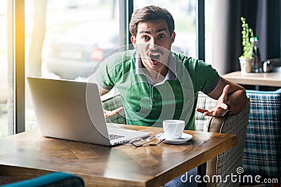 What do you want? Young angry businessman in green t-shirt sitting, looking and screaming at camera with aggressive crazy face Stock Photo