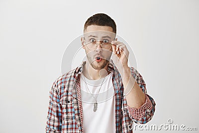 What shocking news you are telling. Portrait amazed office worker holding glasses while wearing it and standing over Stock Photo