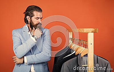 What to choose. Handsome man in smart casual wear looking at suits and choosing. stylish mens clothing on hanger stand Stock Photo
