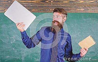What would you prefer. Teacher bearded hipster holds book and laptop. Teacher choosing modern teaching approach. Paper Stock Photo