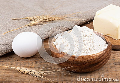 Wheat flour in a wooden bowl, butter and a whole egg on a wooden table. Stock Photo