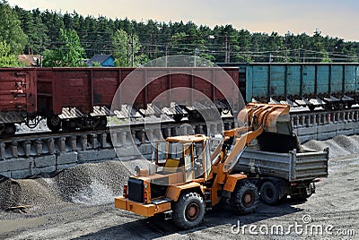 Wheel loader load gravel into a dump truck at a cargo railway station. Fron-end loader unloads crushed stone from gravel pit. Stock Photo