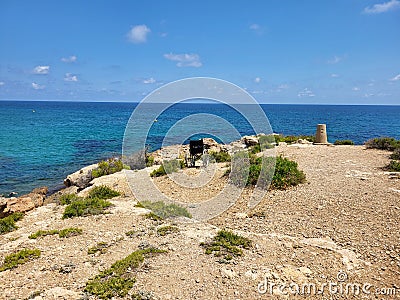 Wheelchair on the beach, rocky coast and sea in a background Stock Photo