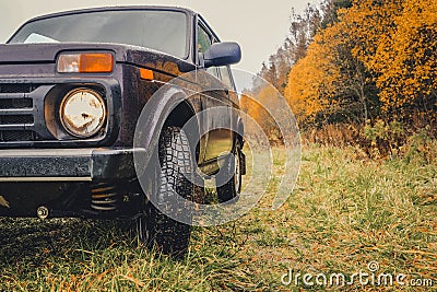 Wheels of an SUV on wet, fading grass at the edge of a forest in the Russian outback on a cloudy autumn day Stock Photo