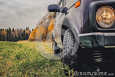 Wheels of an SUV on wet, fading grass at the edge of a forest in the Russian outback on a cloudy autumn day Stock Photo