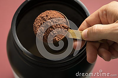 Whey Protein. Perspective of person preparing protein shake. Chocolate flavour. Color background: brown. Stock Photo