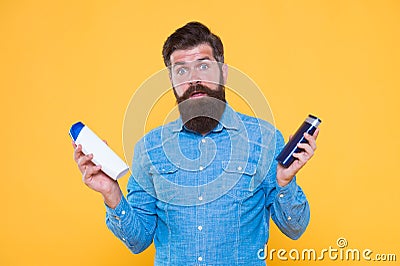 Which soap best. Bearded man hold soap bottles yellow background. Hipster choose liquid soap. For washing in bath or Stock Photo