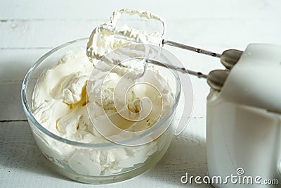 Whipped cream in a bowl and electric hand mixer on bright table. Stock Photo