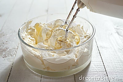 Whipped cream in a bowl and electric hand mixer on bright table. Stock Photo