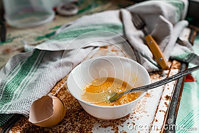 Whipped with a fork and mixed raw egg broken into a white bowl with yolk and protein, next to the shell, fork and towel Stock Photo