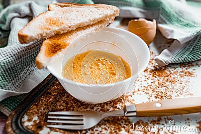 Whipped with a fork and mixed raw egg broken into a white bowl with yolk and protein, next to the shell, fork and towel Stock Photo