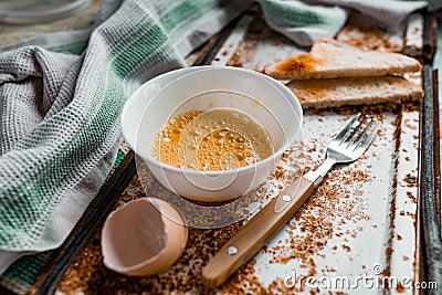 Whipped with a fork and mixed raw egg broken into a white bowl with yolk and protein, next to the shell, fork and towel Stock Photo