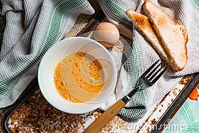 Whipped with a fork and mixed raw egg broken into a white bowl with yolk and protein, next to the shell, fork and towel Stock Photo