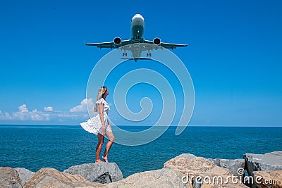 Whirlpool of Wonder: Girl in White Dress, Stones, Blue Sea, and an Airborne Plane Stock Photo