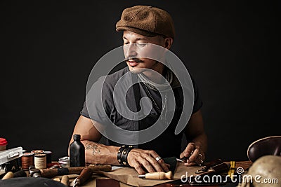 Whiskered shoemaker with making measurments in patterns at table in workshop Stock Photo