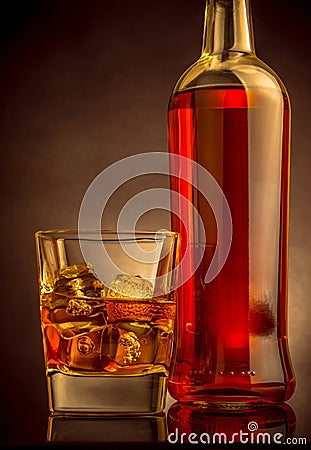 Whiskey with ice cubes in glass near bottle on black background, warm atmosphere Stock Photo