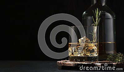 Whiskey, scotch or bourbon glass and bottle with fresh rosemary, ice cubes on black backgroun Stock Photo